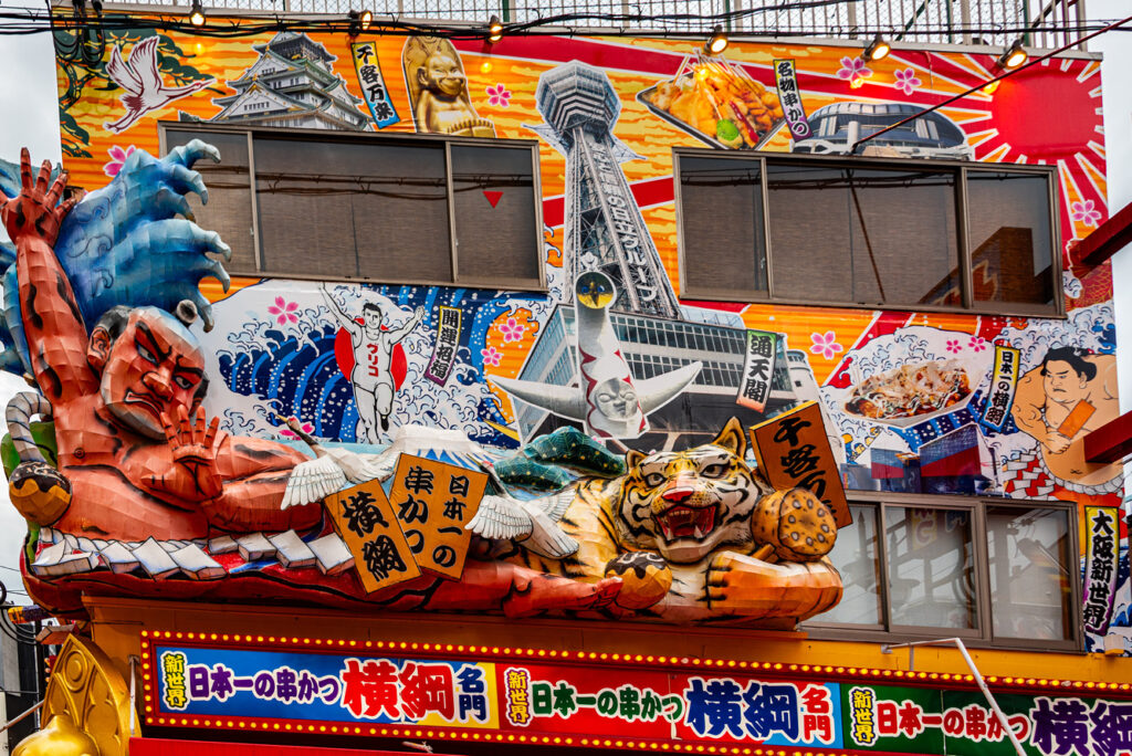 Colorful characters representing Japanese cultural icons jut from a marquee in Osaka’s New World District