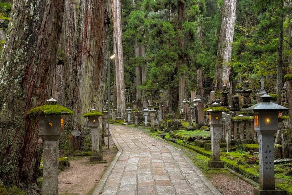Okuno-in’s broad pathway lined with lighted lanterns winds through moss-covered headstones and images