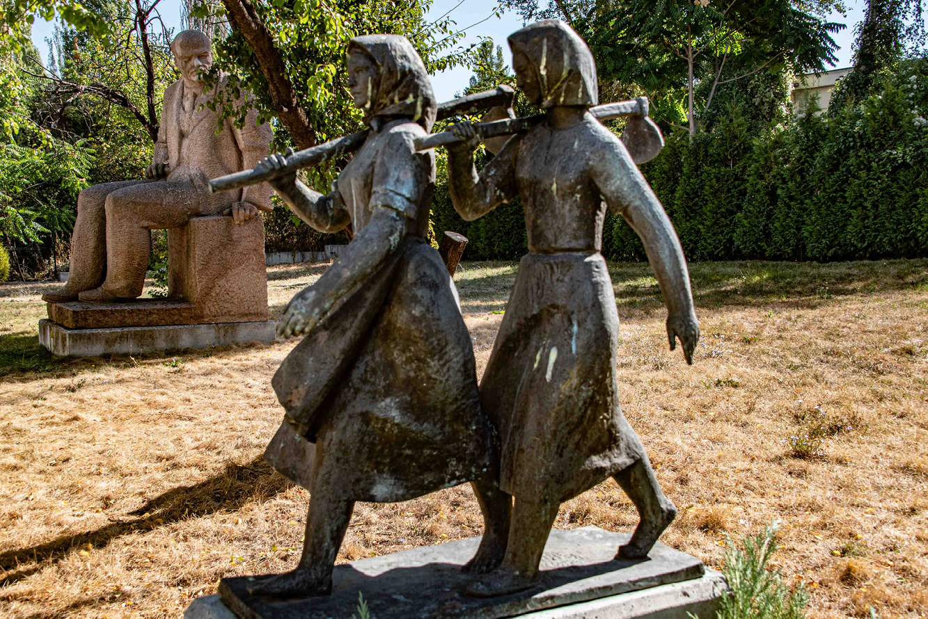 Two peasant women, hoes slung over their shoulders, stride forward to join the revolution